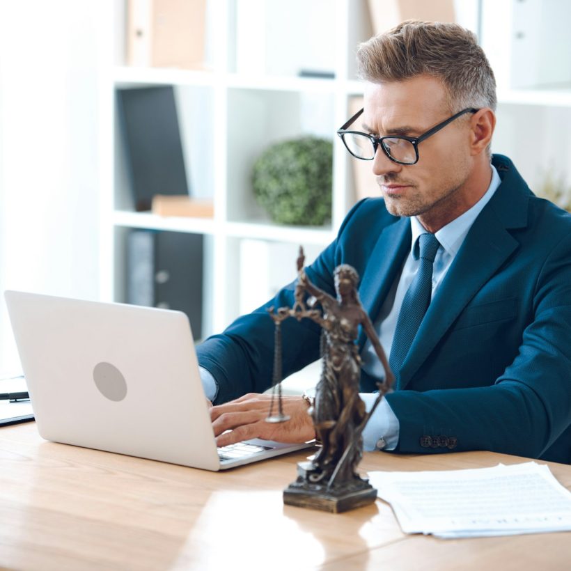 handsome lawyer in eyeglasses using laptop at workplace